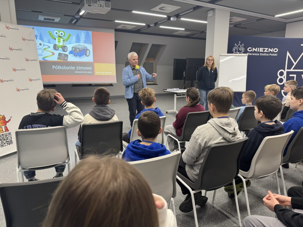 Grupa dzieci patrzących na mężczyznę przemawiającego przez mikrofon.