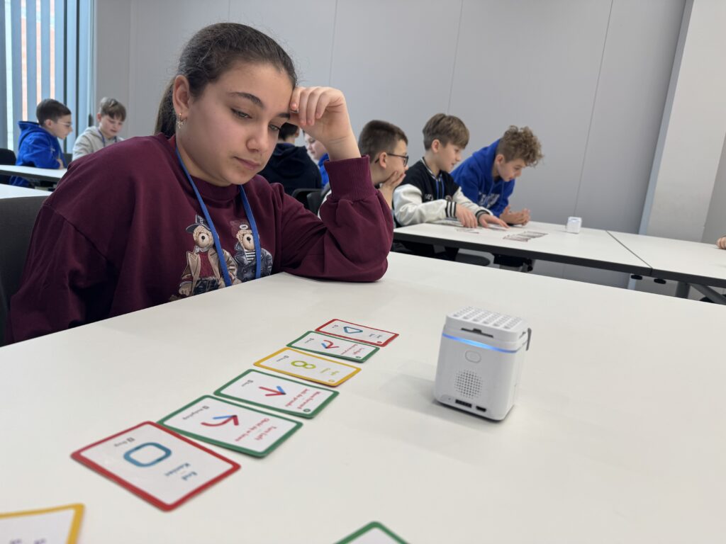 Dziewczynka siedząca przy stole i bawiąca się robotem. 