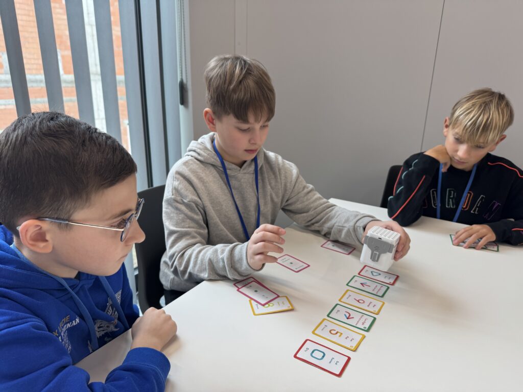 Troje chłopców siedzących przy stole i bawiących się robotem.