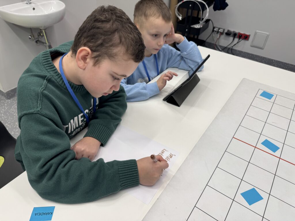 Chłopcy siedzący przy stole i zerkający w tablet. 