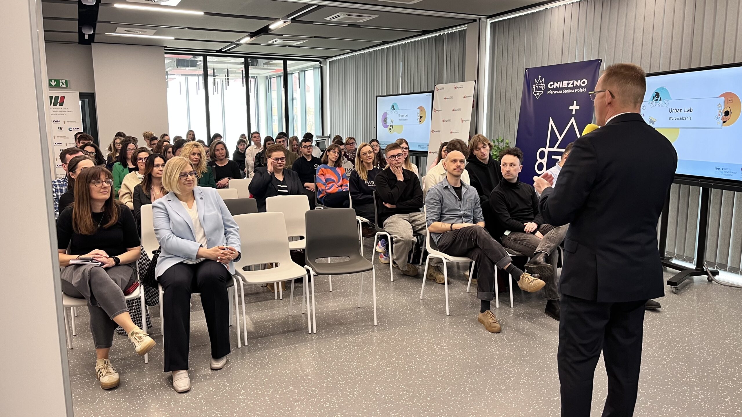 Mężczyzna przemawia, a grupa ludzi słucha.